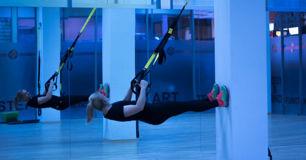 two women doing TRX in a blue lit room two women doing TRX in a blue lit room